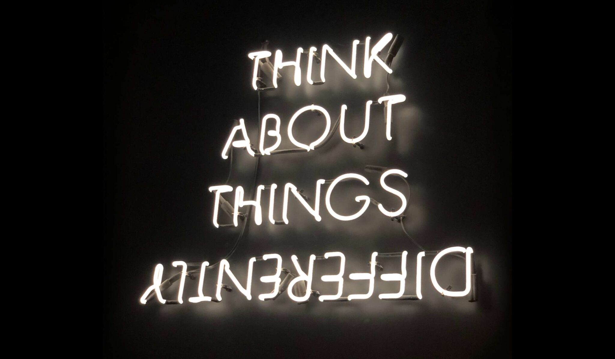 Neon sign with black background reading Think About Things Differently